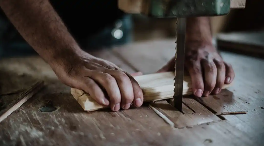 Close up image of a man using a bandsaw to cut a piece of wood